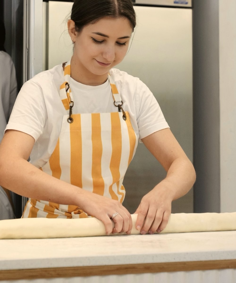 Una panadera enrollando masa en el obrador